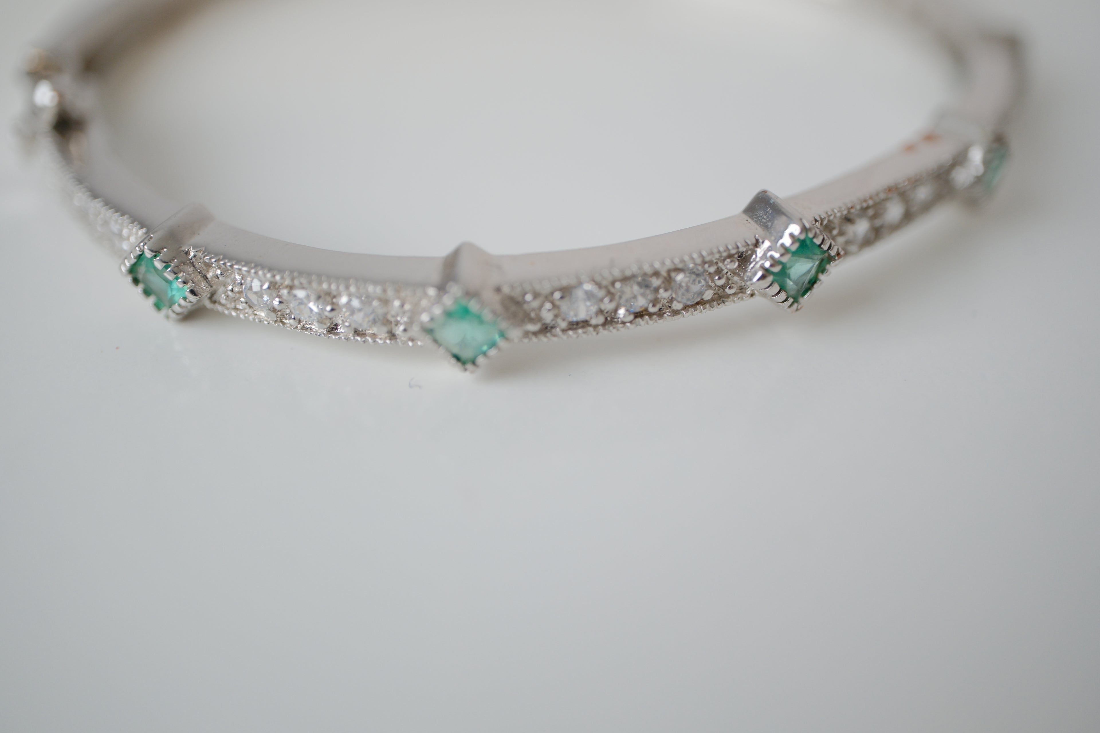 Silver tone bangle bracelet with white and green stones