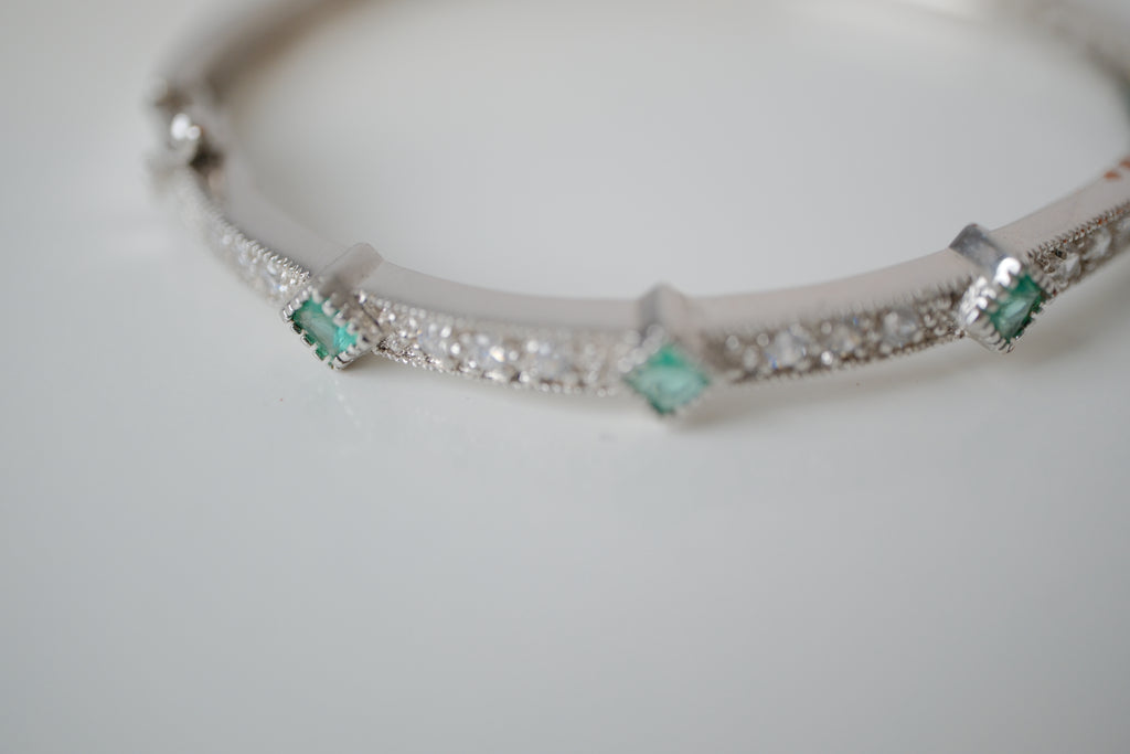 Silver tone bangle bracelet with white and green stones